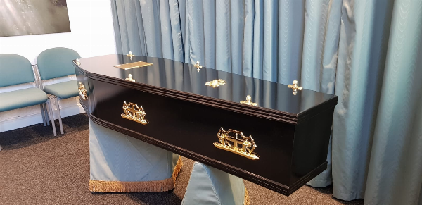 Black Gloss Painted Coffin with gold look burial furnishings. at Jason O'Brien & Family Funeral Services Limited in Ashton-Under-Lyne, Greater Manchester