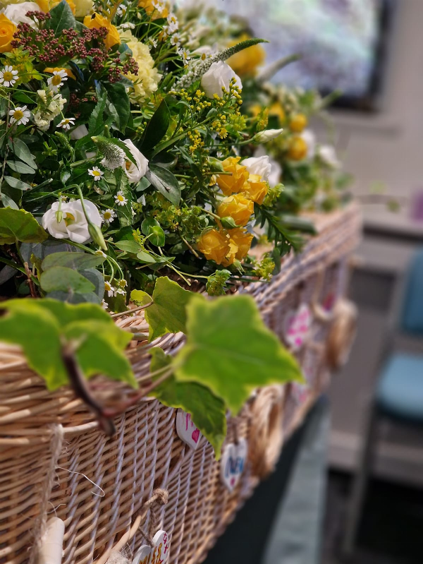 Floral tribute on a light natural willow wicker coffin at Jason O'Brien & Family Funeral Services Limited in Ashton-Under-Lyne, Greater Manchester