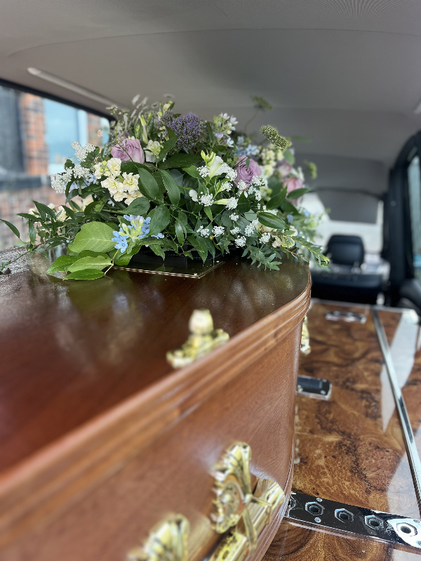 Coffin in the hearse adorned with funeral flowers at Jason O'Brien & Family Funeral Services Limited in Ashton-Under-Lyne, Greater Manchester #Hearse #Funeral #Floraltribute #Mahoganyveneercoffin